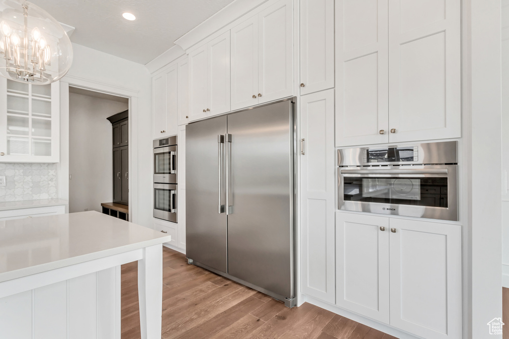 Kitchen with appliances with stainless steel finishes, an inviting chandelier, white cabinetry, and light wood-type flooring