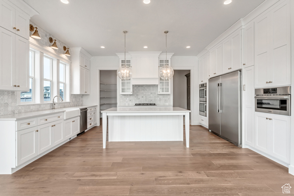 Kitchen featuring backsplash, stainless steel appliances, white cabinetry, light hardwood / wood-style flooring, and a kitchen island