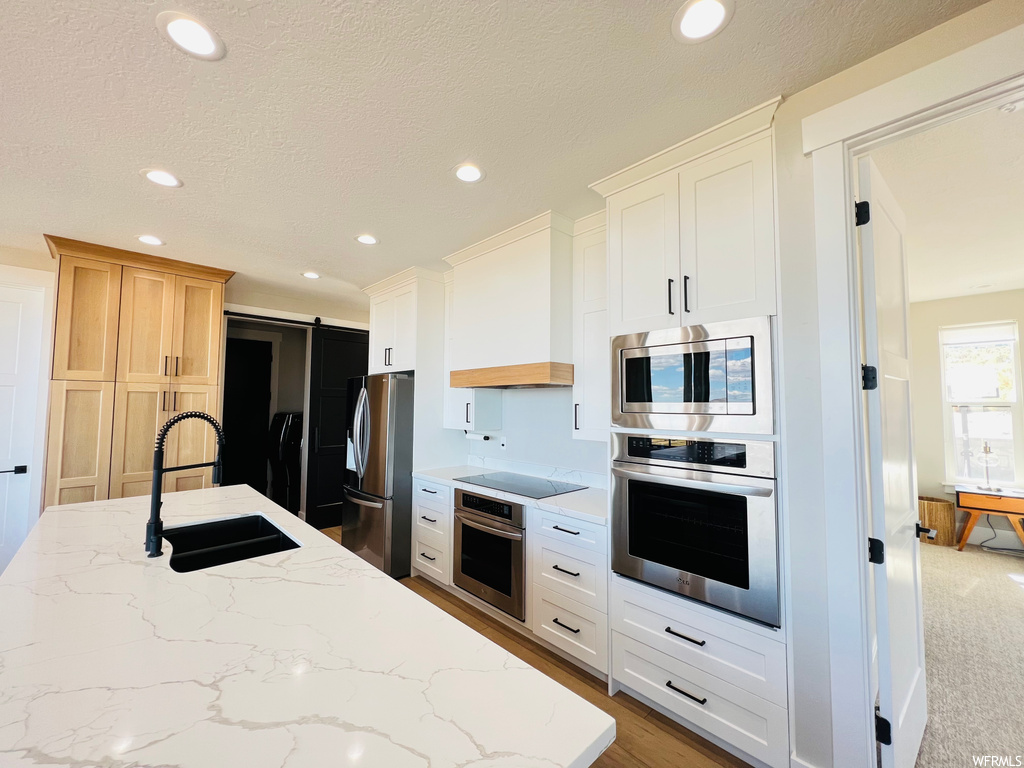 Kitchen featuring appliances with stainless steel finishes, custom range hood, a textured ceiling, white cabinets, light stone countertops, and light carpet