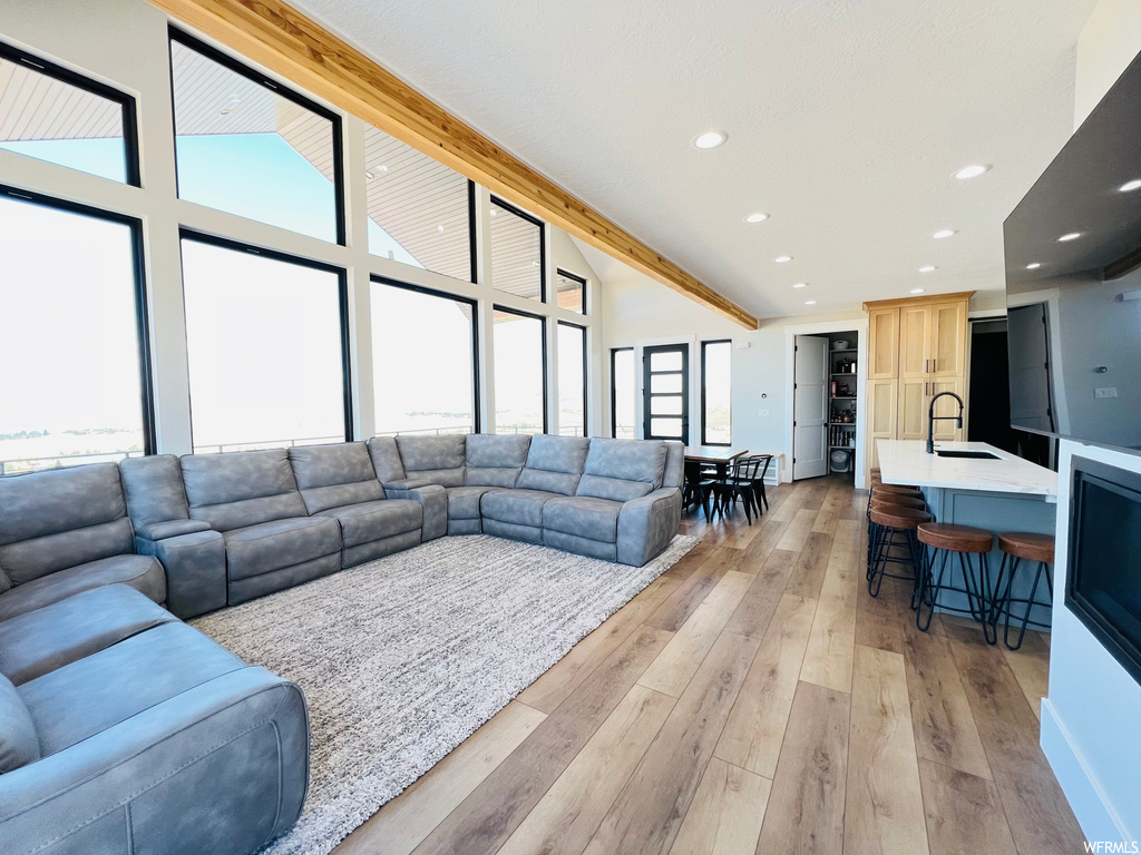 Living room featuring light hardwood floors, beamed ceiling, and a high ceiling