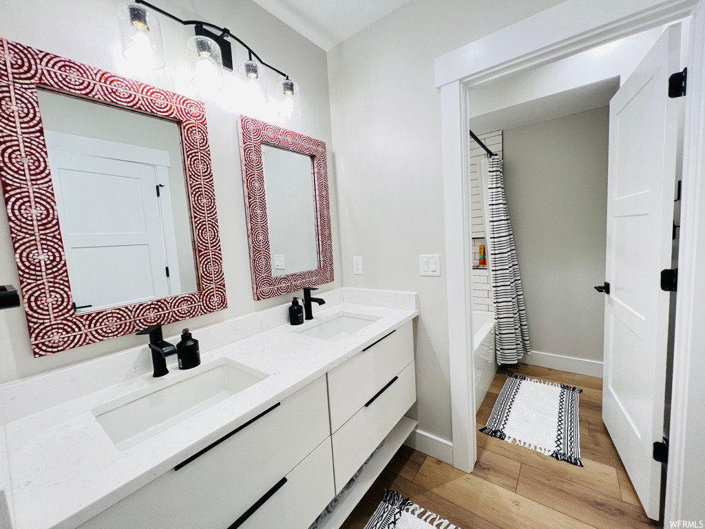 Bathroom with shower / bath combo with shower curtain, double large vanity, light hardwood floors, and mirror
