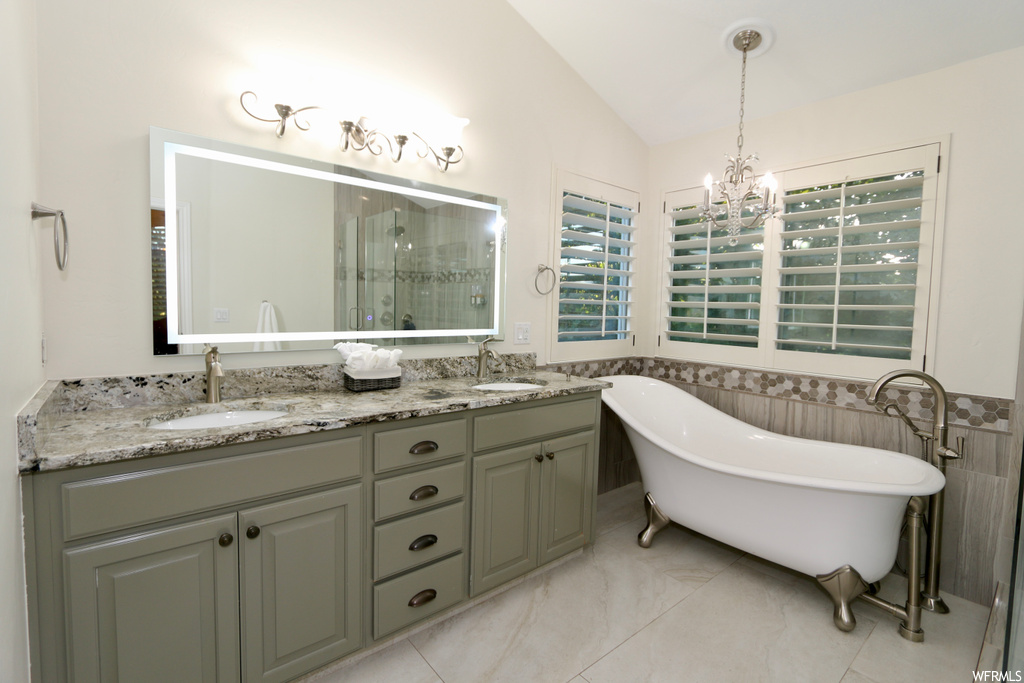 Bathroom featuring mirror, dual vanity, lofted ceiling, a bath to relax in, and light tile floors