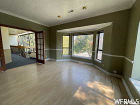Unfurnished room with a textured ceiling, light hardwood floors, and crown molding