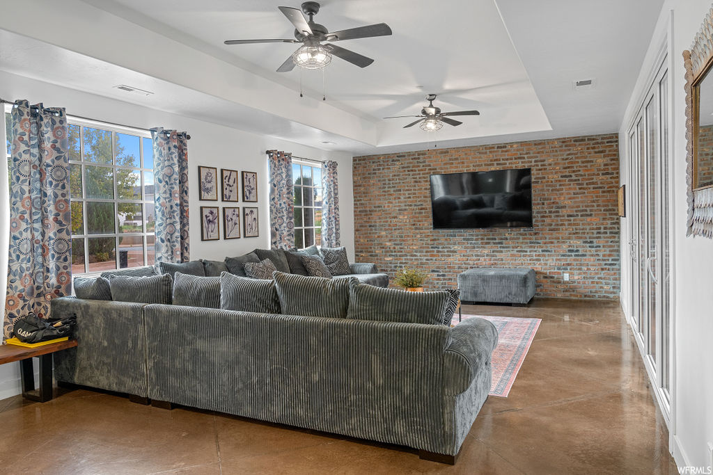 Living room with brick wall, a raised ceiling, and ceiling fan