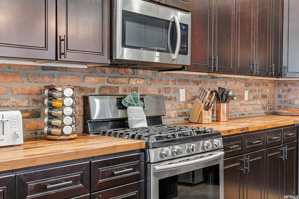 Kitchen featuring light countertops, dark brown cabinetry, brick wall, and appliances with stainless steel finishes