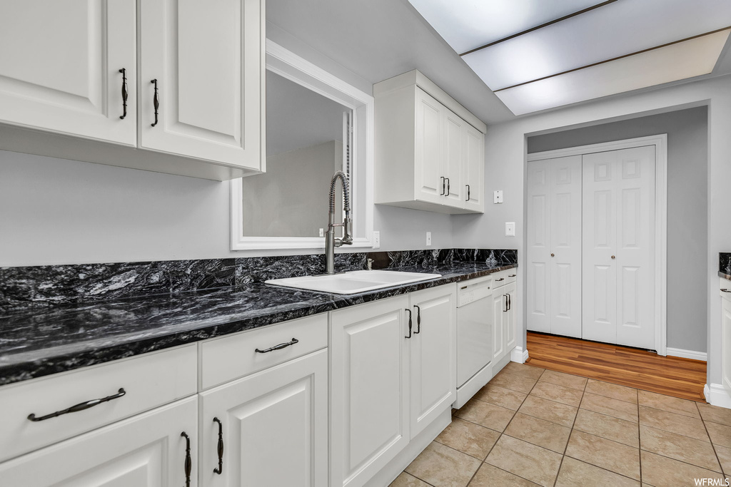 Kitchen with dark stone countertops, white cabinets, white dishwasher, and light tile flooring