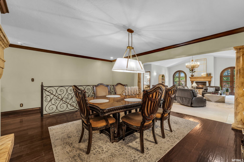 Hardwood floored dining area with a notable chandelier, ornamental molding, and a fireplace