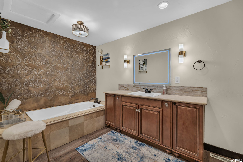 Bathroom with vanity, mirror, hardwood flooring, backsplash, and tiled bath