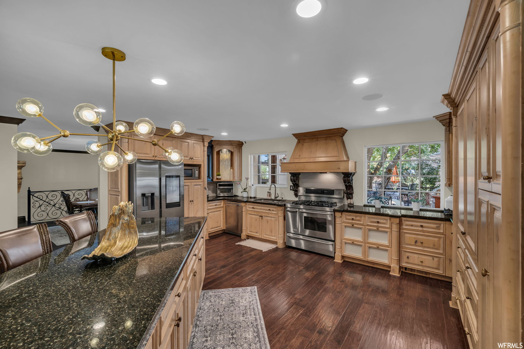 Kitchen featuring stainless steel appliances, dark stone counters, dark hardwood floors, brown cabinets, and premium range hood