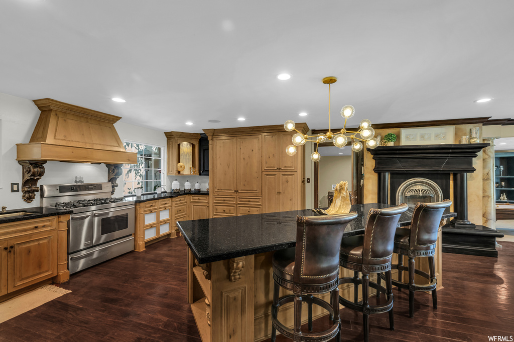Kitchen featuring a center island, dark countertops, dark hardwood floors, custom exhaust hood, brown cabinets, stainless steel range with gas cooktop, and ornamental molding
