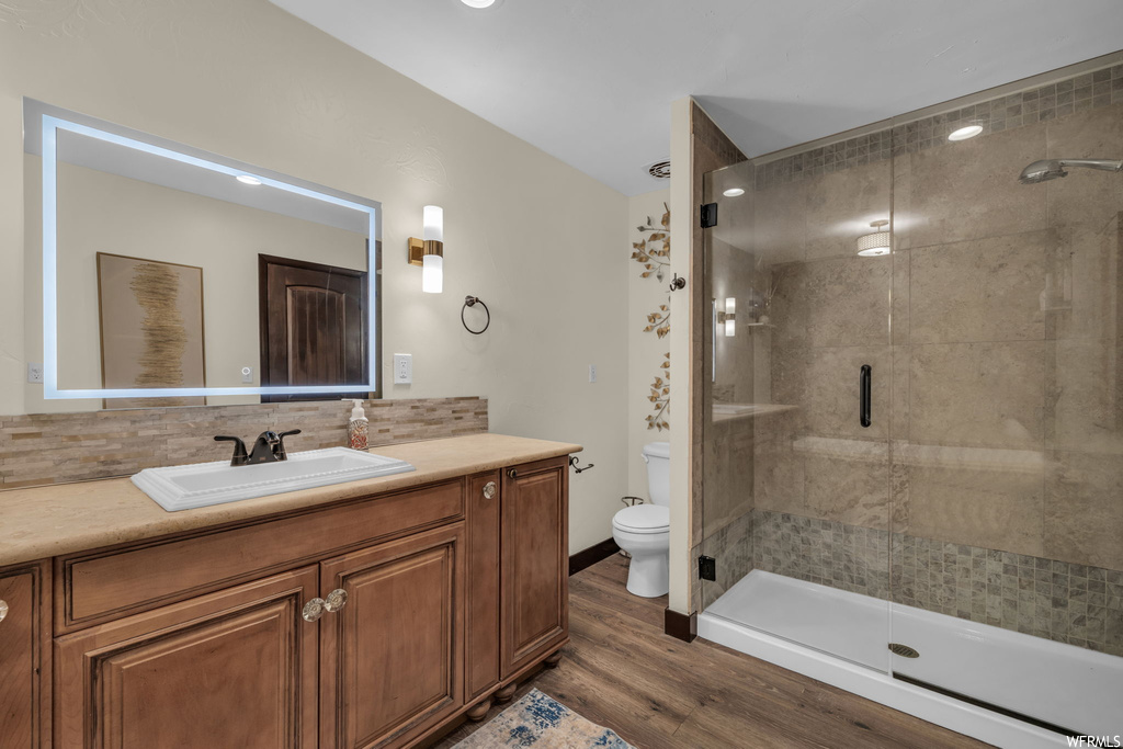 Bathroom featuring vanity with extensive cabinet space, backsplash, mirror, hardwood floors, and an enclosed shower