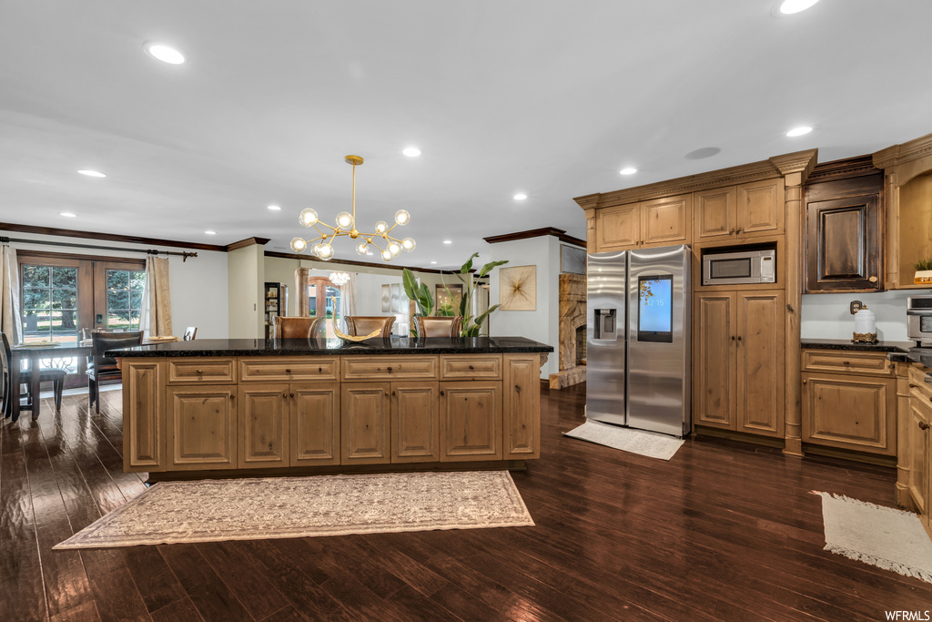 Kitchen with appliances with stainless steel finishes, brown cabinets, crown molding, and dark hardwood flooring