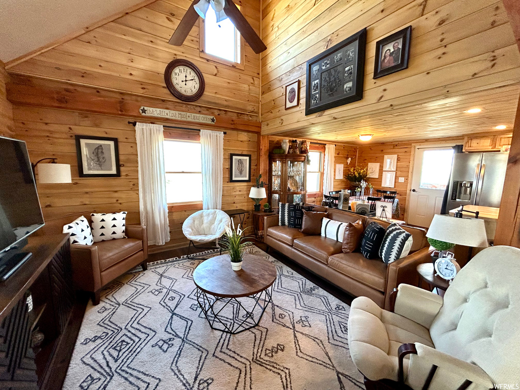 Living room with plenty of natural light, lofted ceiling, ceiling fan, wooden walls, and a high ceiling