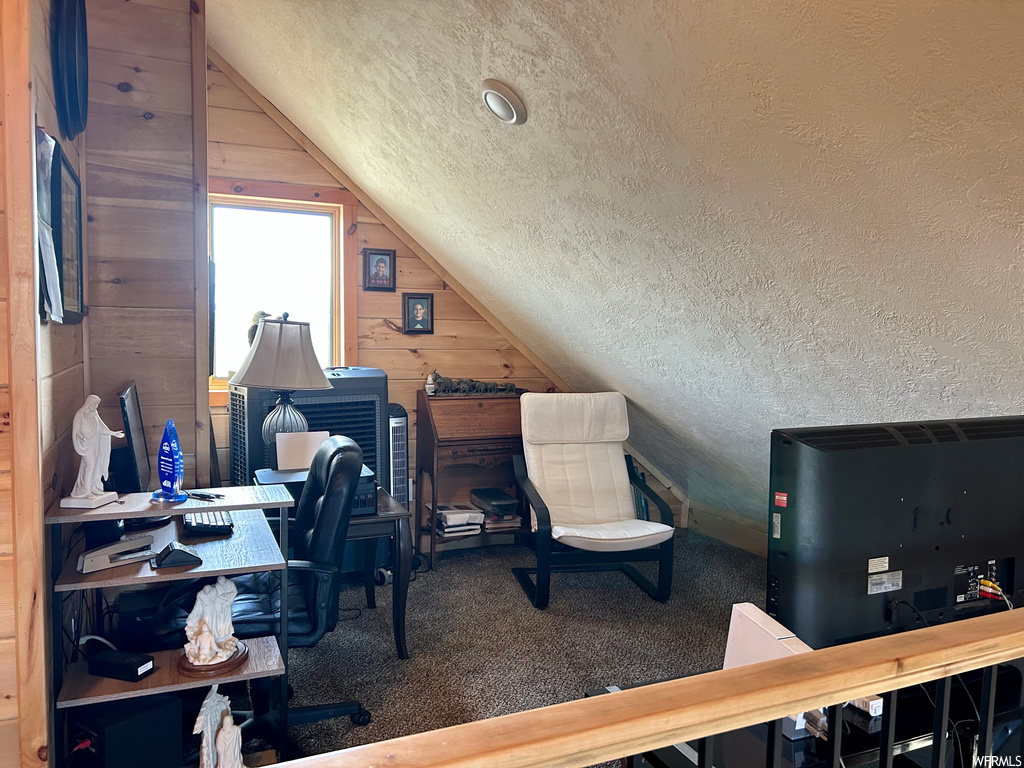 Office with wooden walls, a textured ceiling, vaulted ceiling, and carpet
