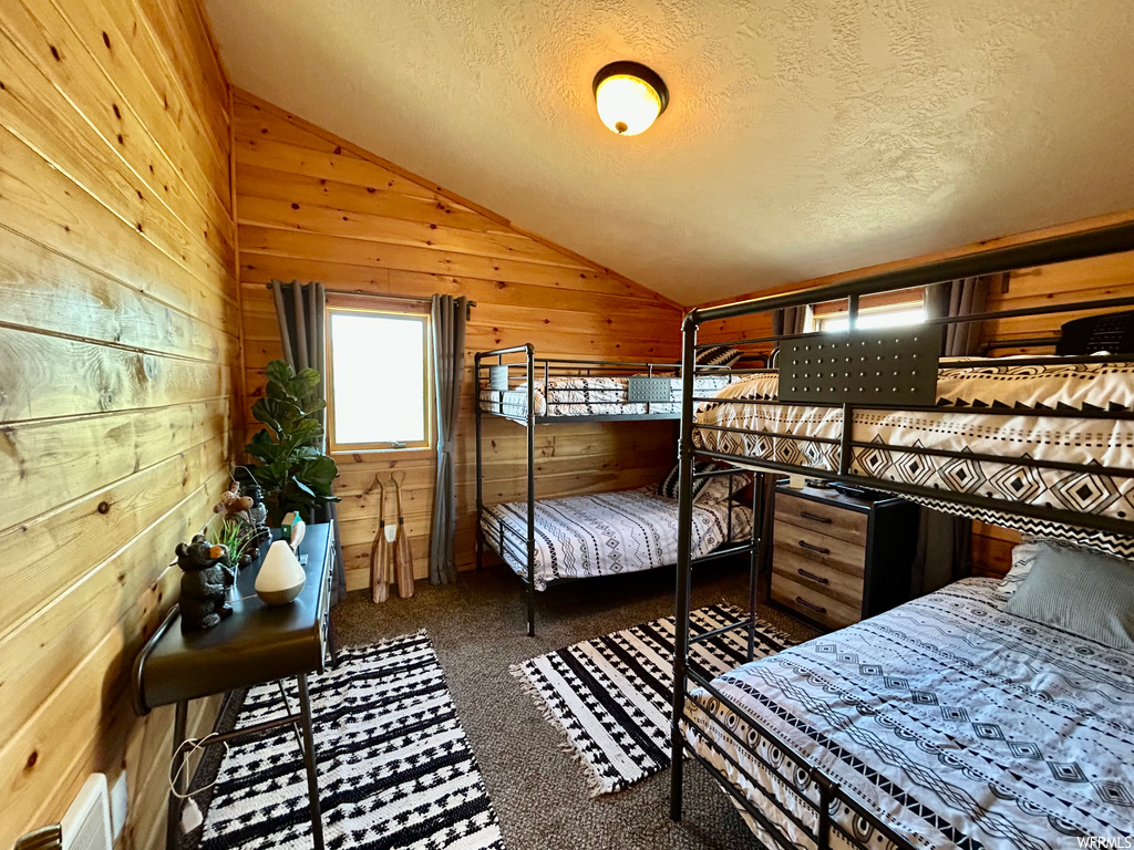 Bedroom featuring wooden walls, dark carpet, vaulted ceiling, and a textured ceiling