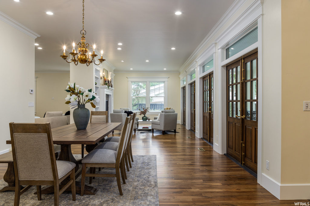 Dining space featuring dark hardwood floors, a fireplace, ornamental molding, and a chandelier