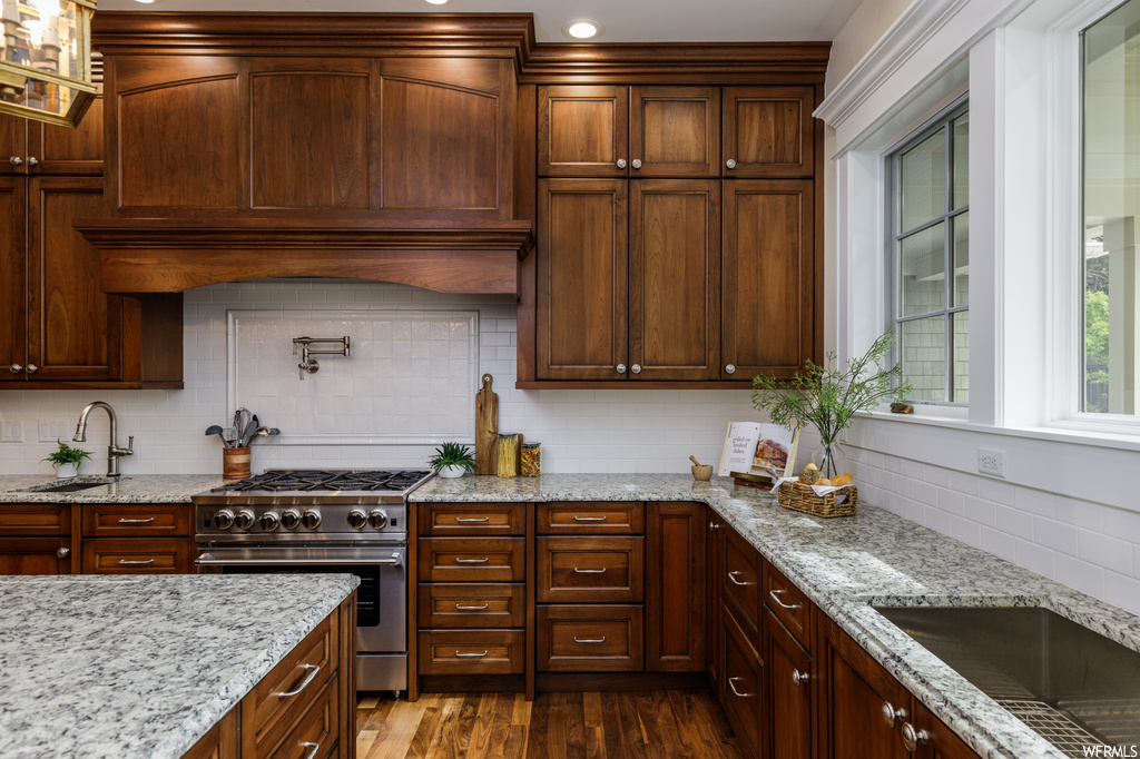 Kitchen featuring high end stainless steel range oven, custom exhaust hood, light stone countertops, wood-type flooring, dark brown cabinets, and backsplash