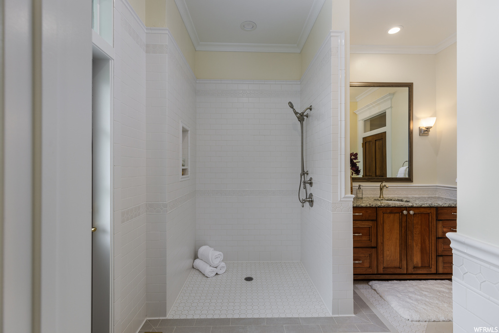 Bathroom with tiled shower, vanity with extensive cabinet space, mirror, crown molding, and light tile flooring