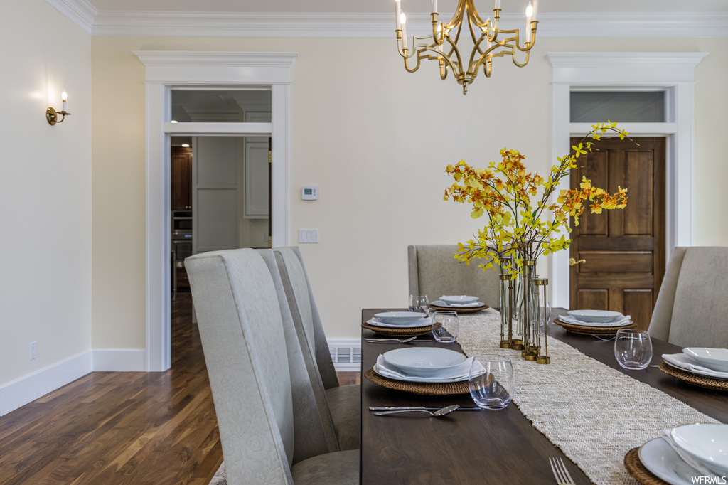 Hardwood floored dining room featuring crown molding and a notable chandelier