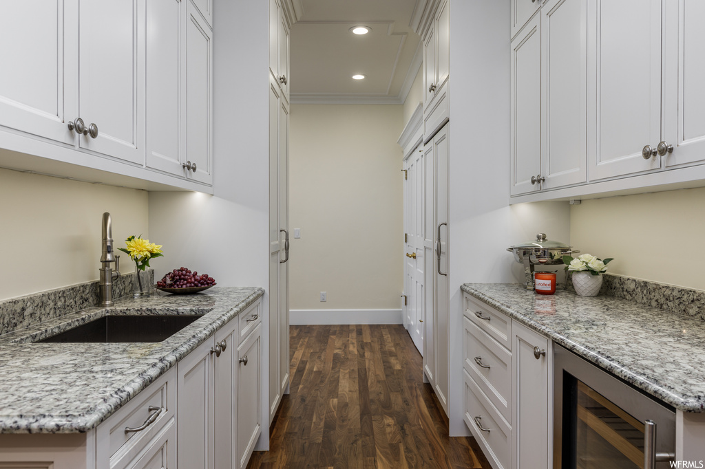 Kitchen featuring crown molding, light stone countertops, white cabinets, and dark hardwood floors