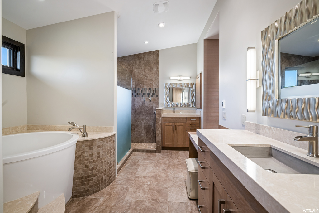 Bathroom featuring double large vanity, light tile flooring, mirror, a wealth of natural light, and independent shower and bath