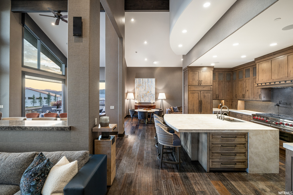 Kitchen featuring backsplash, premium range, light countertops, ceiling fan, dark hardwood flooring, a high ceiling, and range hood