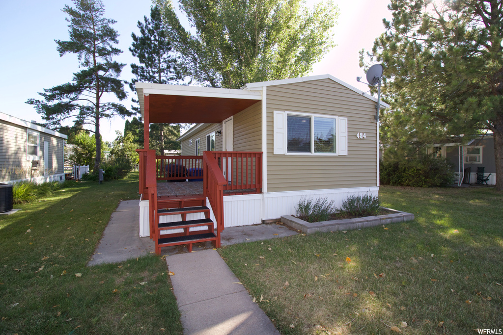 View of front of property featuring central air condition unit, a deck, and a front yard