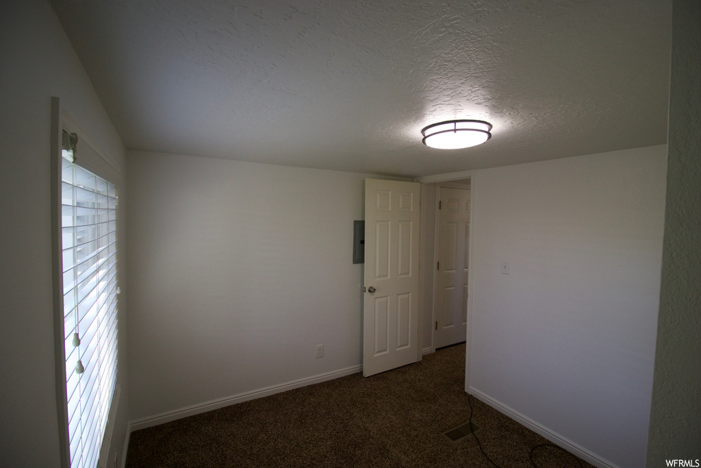 Empty room featuring a textured ceiling, a wealth of natural light, and dark carpet