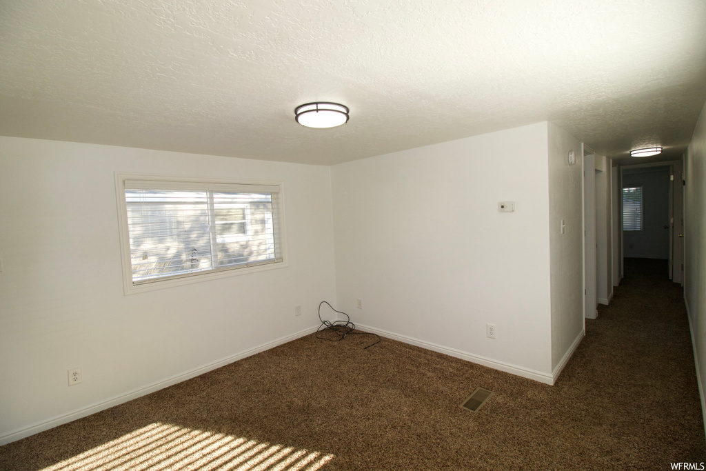 Empty room featuring a textured ceiling and dark carpet