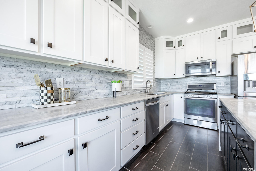 Kitchen with light stone counters, stainless steel appliances, backsplash, and white cabinetry
