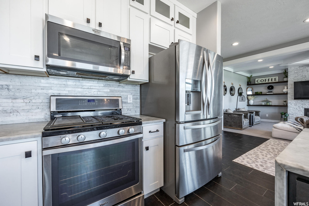 Kitchen featuring stainless steel appliances, white cabinetry, dark hardwood flooring, light countertops, and backsplash