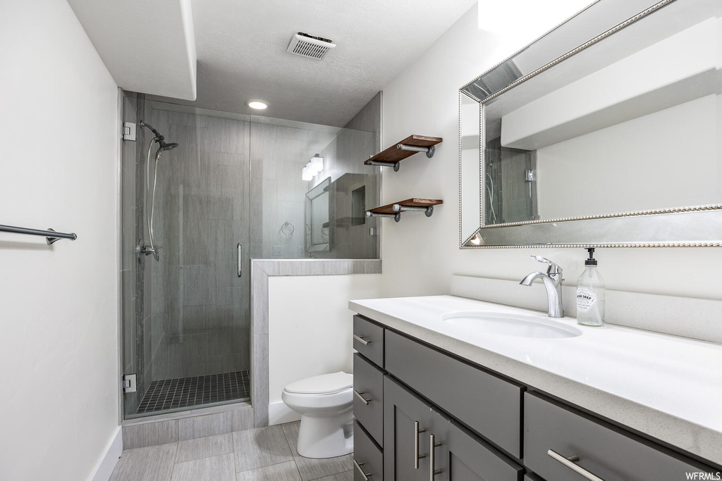 Bathroom featuring an enclosed shower, vanity with extensive cabinet space, mirror, and light tile floors