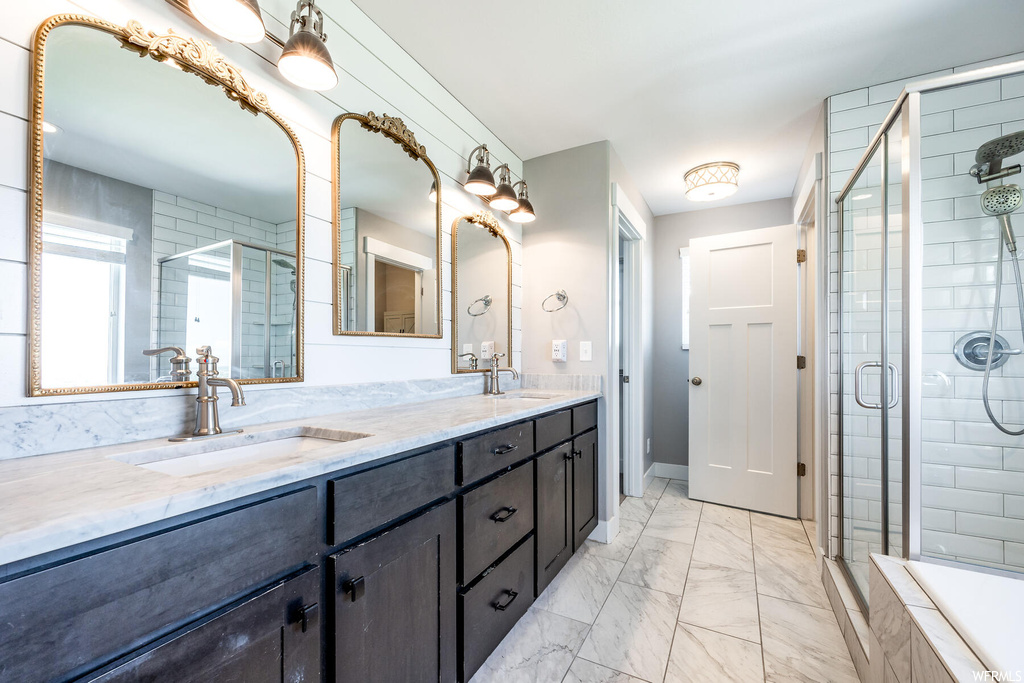 Bathroom featuring a shower with shower door, double sink vanity, mirror, and light tile flooring