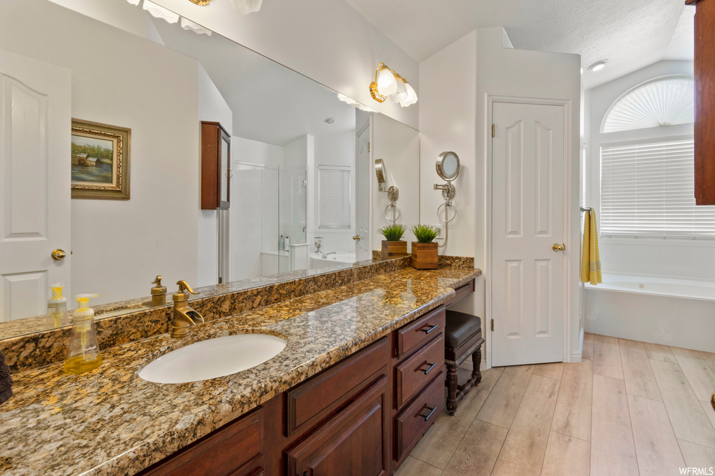Bathroom with a textured ceiling, vanity with extensive cabinet space, mirror, vaulted ceiling, independent shower and bath, and light hardwood flooring