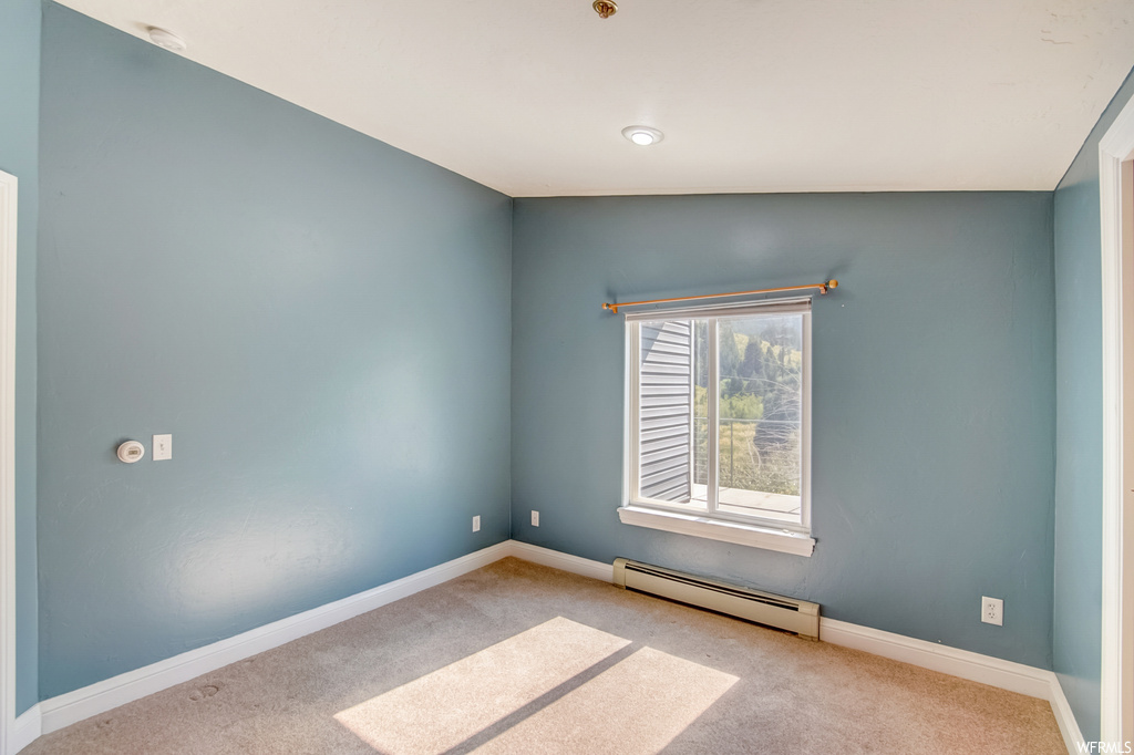 Empty room with a baseboard heating unit, light carpet, and lofted ceiling