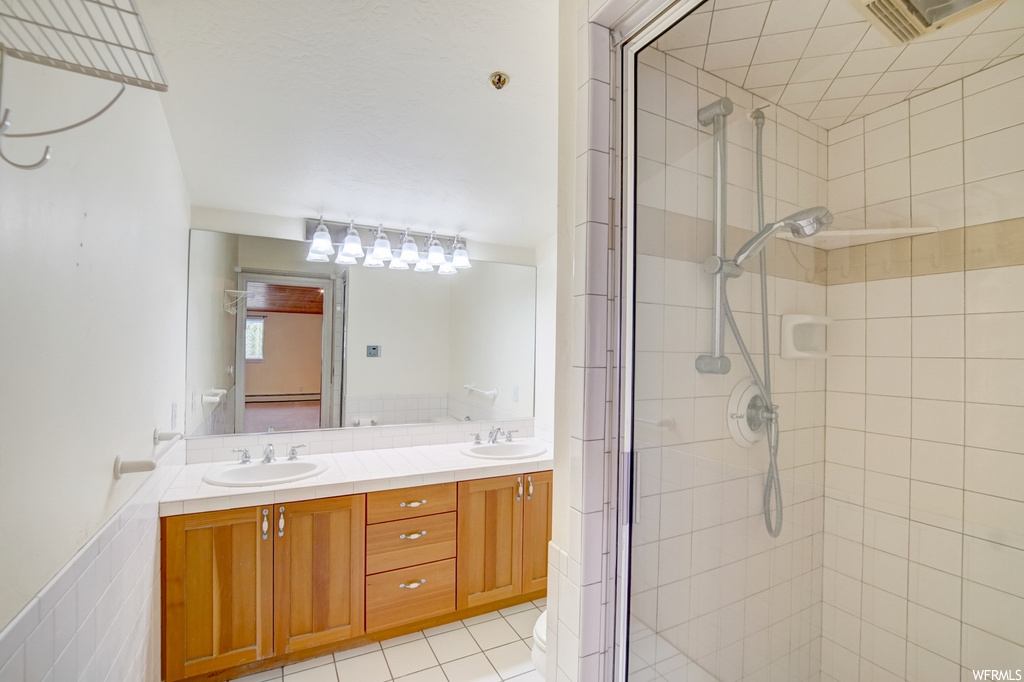 Bathroom featuring dual vanity, a shower with shower door, mirror, and light tile floors
