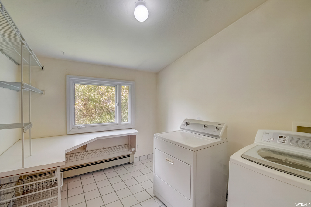 Laundry room with washing machine and clothes dryer, a baseboard radiator, and light tile flooring