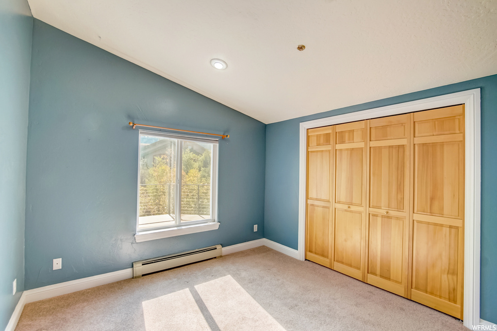 Bedroom with light carpet, vaulted ceiling, and baseboard heating