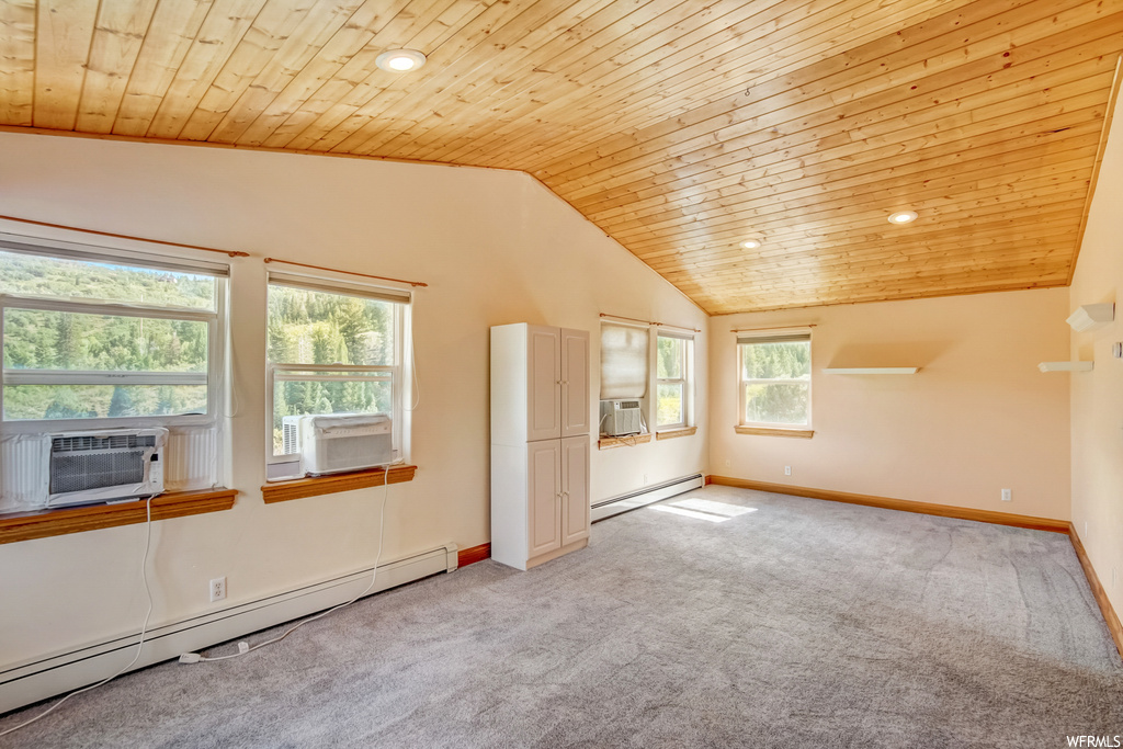 Carpeted empty room featuring vaulted ceiling, baseboard heating, wood ceiling, and plenty of natural light