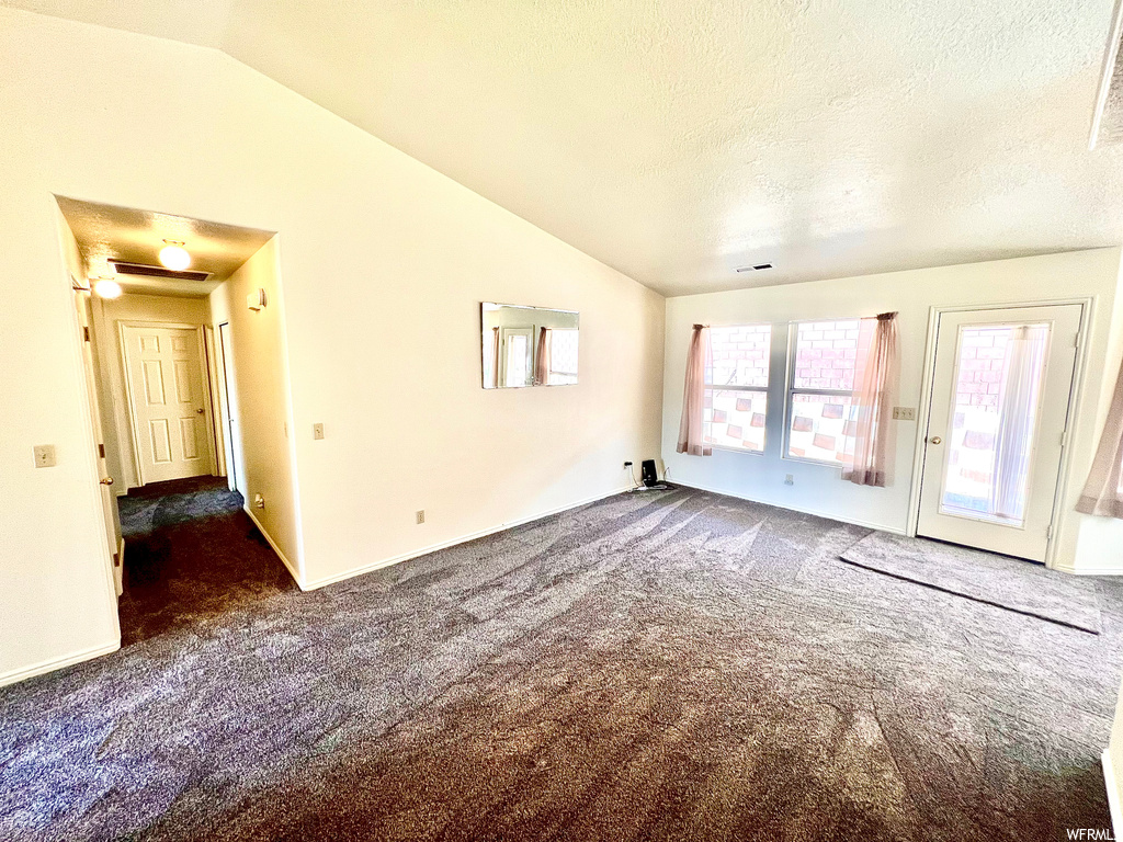 Unfurnished room featuring light carpet, lofted ceiling, and a textured ceiling