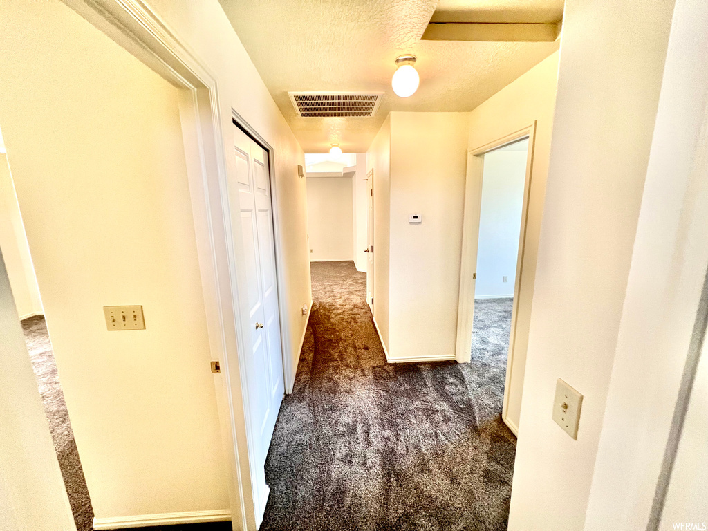 Corridor featuring a textured ceiling and dark carpet