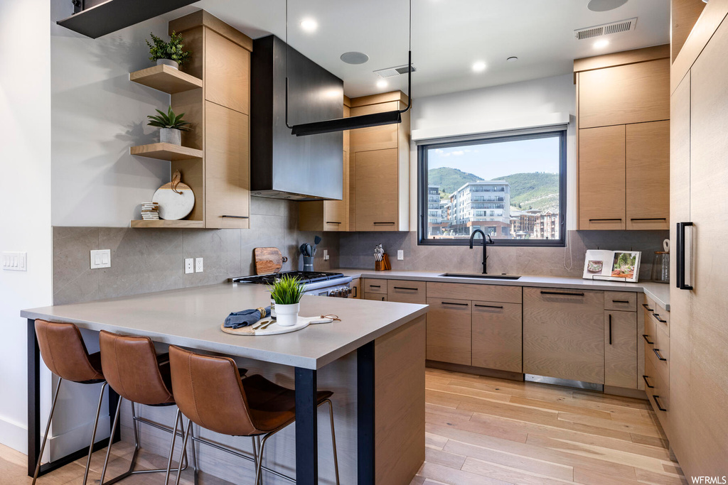 Kitchen with wall chimney range hood, a center island, dishwasher, range, light countertops, light hardwood flooring, and backsplash