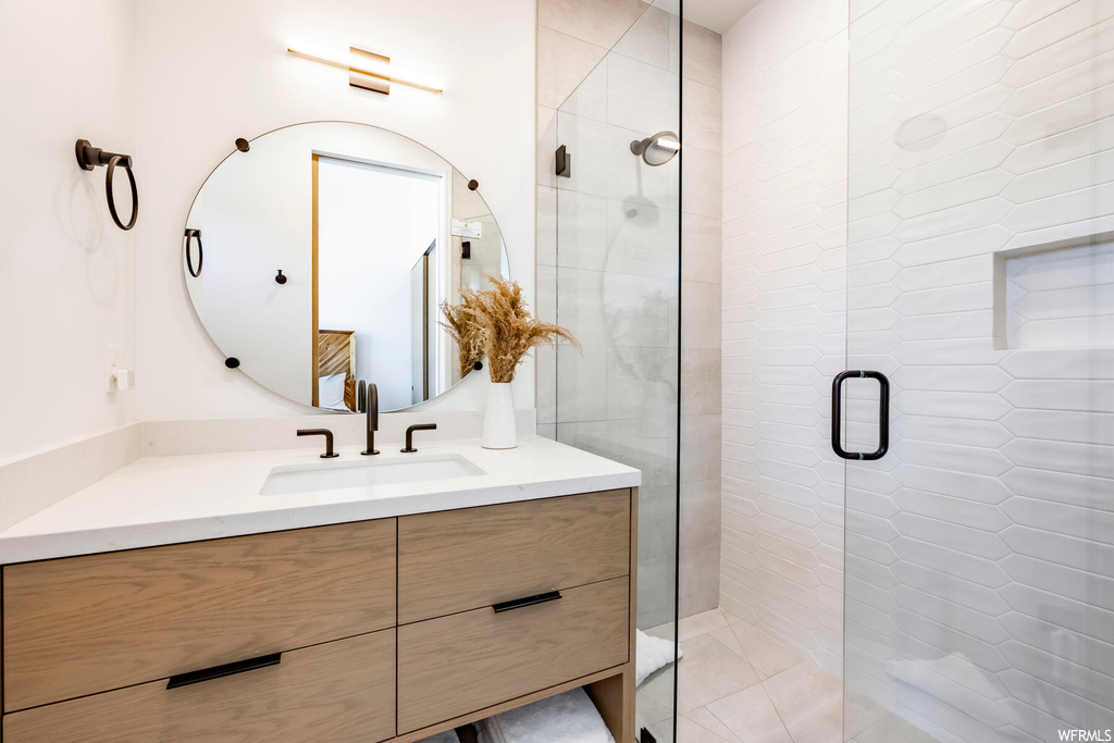 Bathroom featuring vanity with extensive cabinet space, a shower with shower door, and mirror