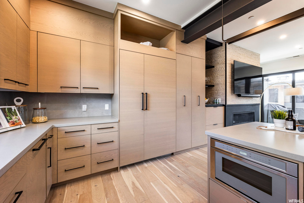 Kitchen featuring stainless steel oven, light countertops, light hardwood flooring, backsplash, and beam ceiling