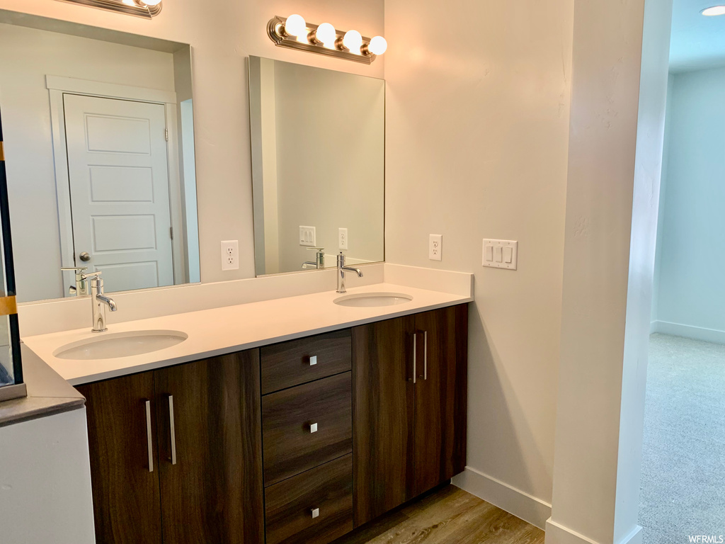 Bathroom featuring light hardwood flooring, mirror, and dual bowl vanity