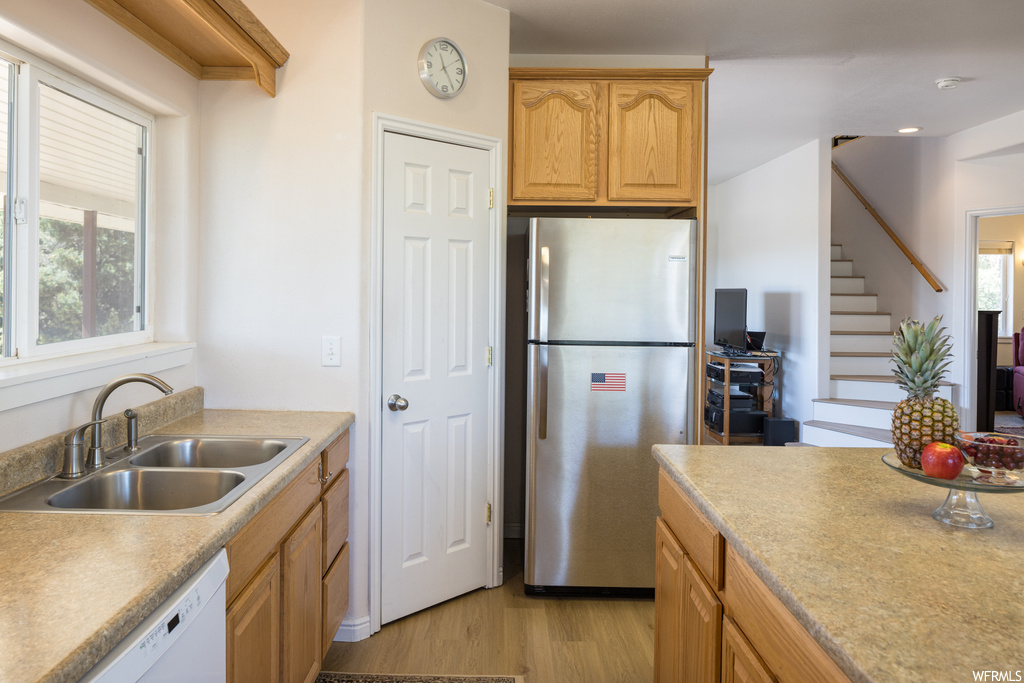 Kitchen featuring stainless steel refrigerator, brown cabinets, light countertops, light hardwood floors, and white dishwasher