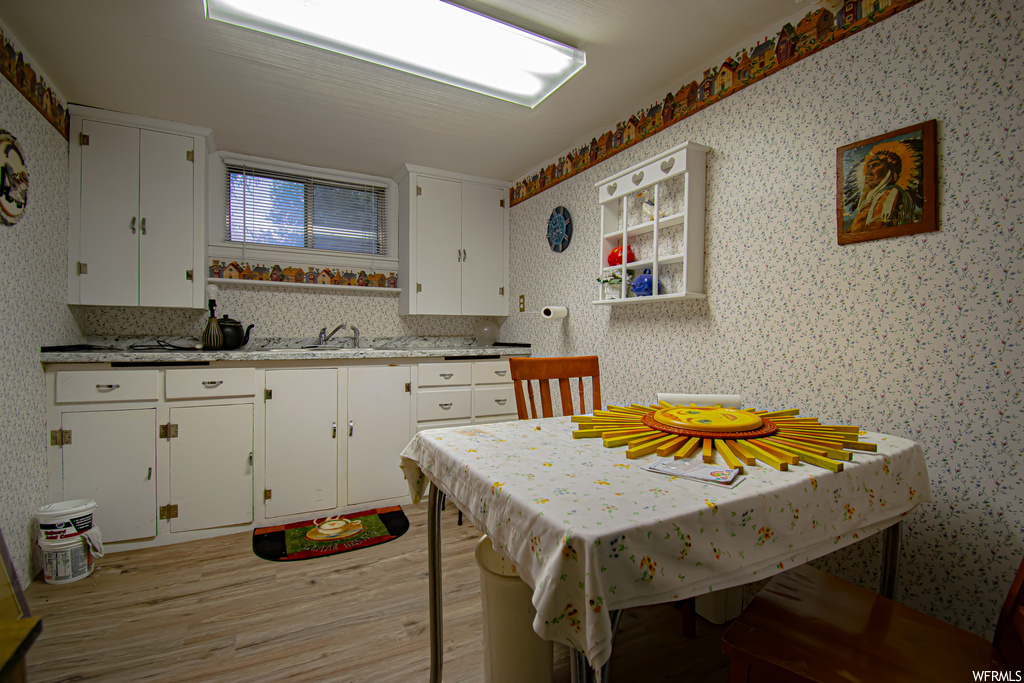 Kitchen with light hardwood / wood-style floors, sink, light stone countertops, backsplash, and white cabinets