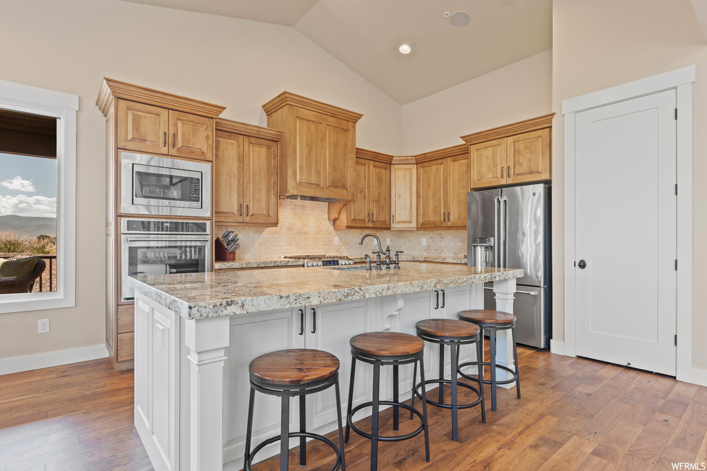 Kitchen featuring appliances with stainless steel finishes, a kitchen island, lofted ceiling, light stone counters, light hardwood flooring, and backsplash