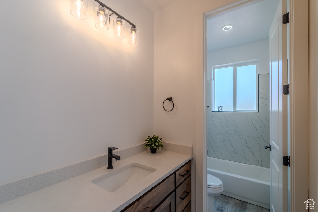 Full bathroom with hardwood / wood-style floors, vanity, tiled shower / bath combo, and toilet