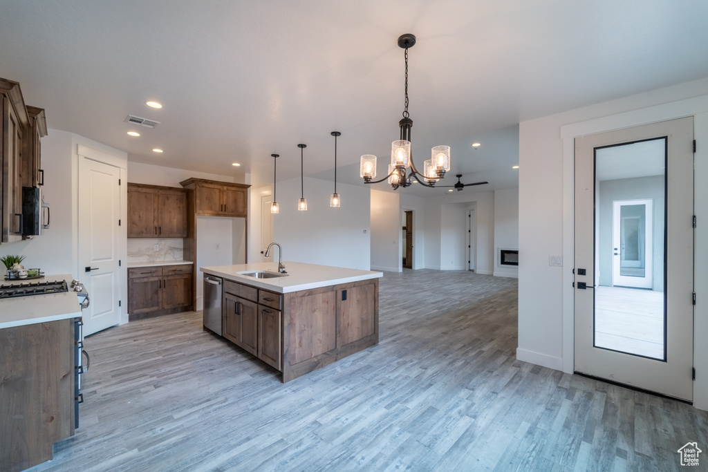 Kitchen featuring dishwasher, a center island with sink, light wood-type flooring, hanging light fixtures, and sink